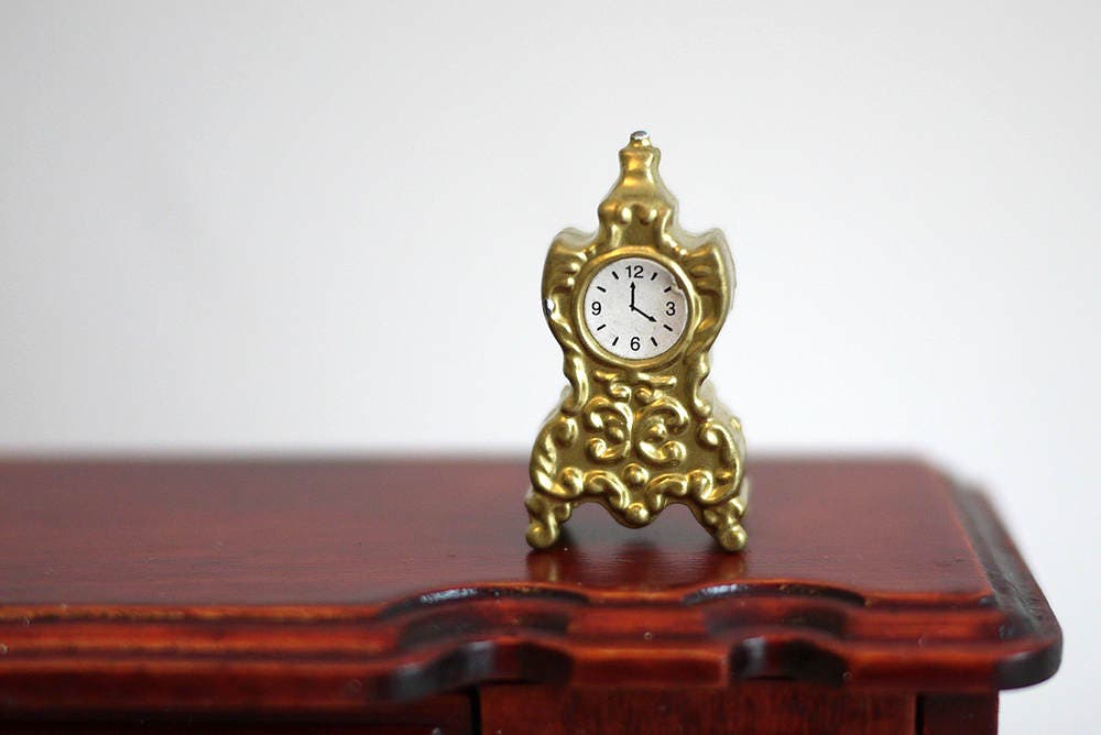 1:12 scale miniature metal anniversary clock in gold with ornate scroll case, non working, on a dark wood table