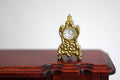 1:12 scale miniature metal anniversary clock in gold with ornate scroll case, non working, on a dark wood table