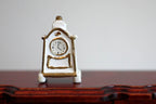 1:12 scale miniature ceramic tabletop anniversary clock in white with gold trim, non working, shown on a dark wood table