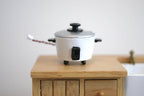 1:12 scale miniature rice cooker in white with black lid knob, handles and cord, shown on a wood kitchen cabinet