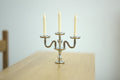 1:12 scale miniature candelabra in silver, 3 arms with cream candles, shown on a light wood table