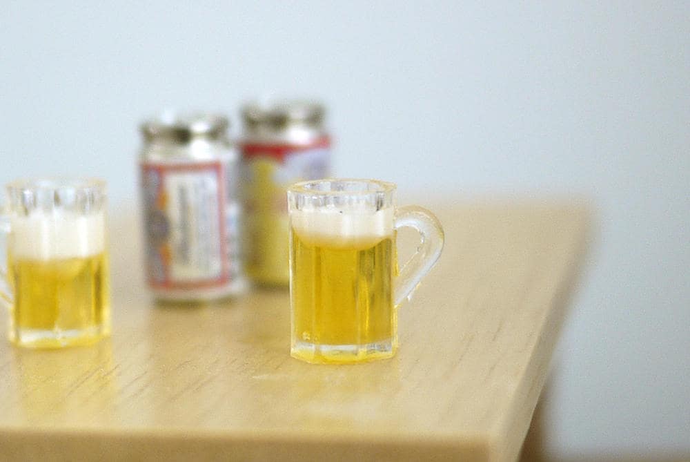 1:12 scale miniature beer mug with foam top, clear handled mug with golden beer, shown on a wood table with cans