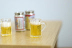 1:12 scale miniature beer mug with foam top, clear handled mug with golden beer, shown on a wood table with cans