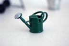 1:12 scale miniature metal watering can in dark green with spray nozzle and loop handles, on a white surface