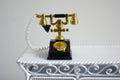 1:12 scale miniature metal rotary dial telephone in black and gold with white cord, shown on a white ornate table