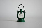 1:12 scale miniature metal hurricane oil lantern in green with wire handle and white globe, on a gray background