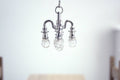 1:12 scale miniature metal chandelier in silver with 4 arms and clear bulbs, non-electric, shown hanging