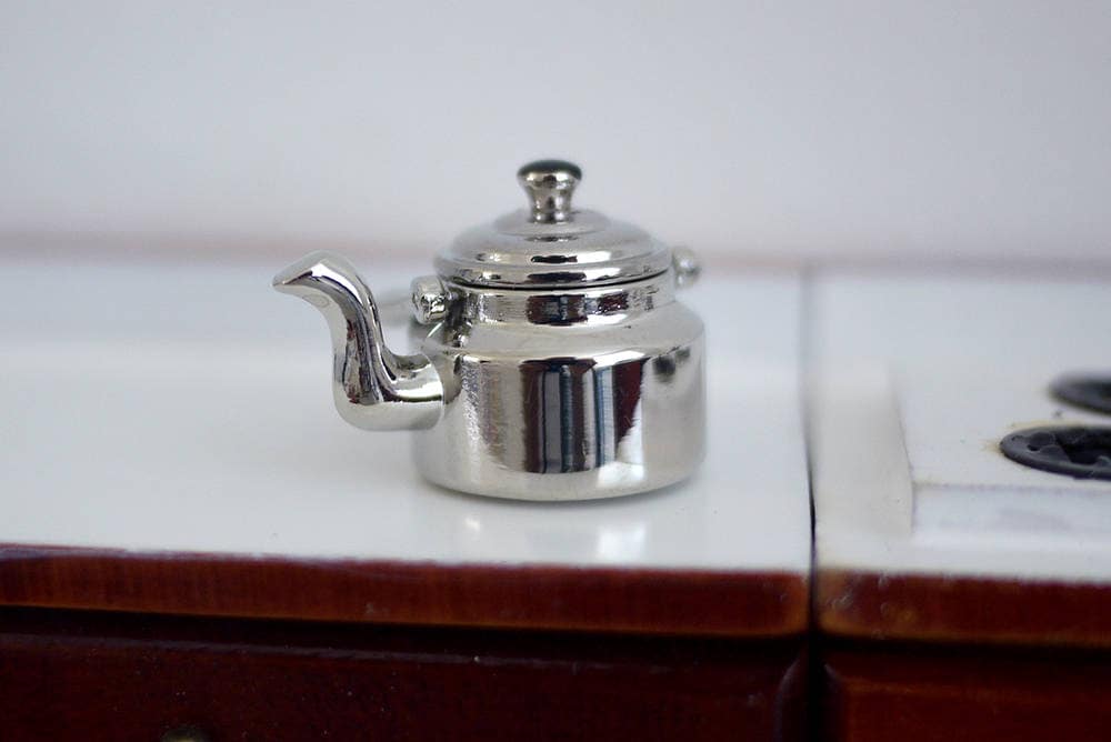 1:12 scale miniature metal kettle with lid in polished silver with curved spout, shown on a white stovetop