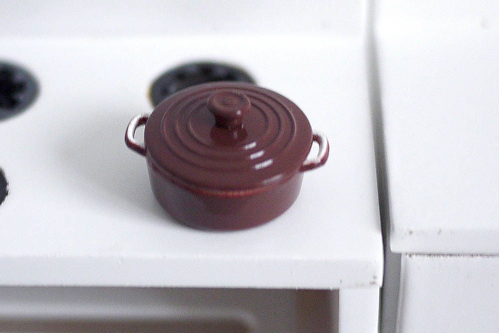 1:12 scale miniature metal cooking pot with lid in burgundy with side handles, shown on a white stove top