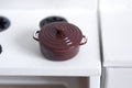 1:12 scale miniature metal cooking pot with lid in burgundy with side handles, shown on a white stove top