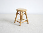 1:12 scale miniature wood round stool in honey finish with 4 turned legs and rungs, shown on a white surface