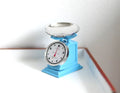 1:12 scale miniature retro kitchen scale in light blue with round dial and silver bowl, shown on a white surface