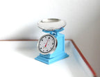 1:12 scale miniature retro kitchen scale in light blue with round dial and silver bowl, shown on a white surface