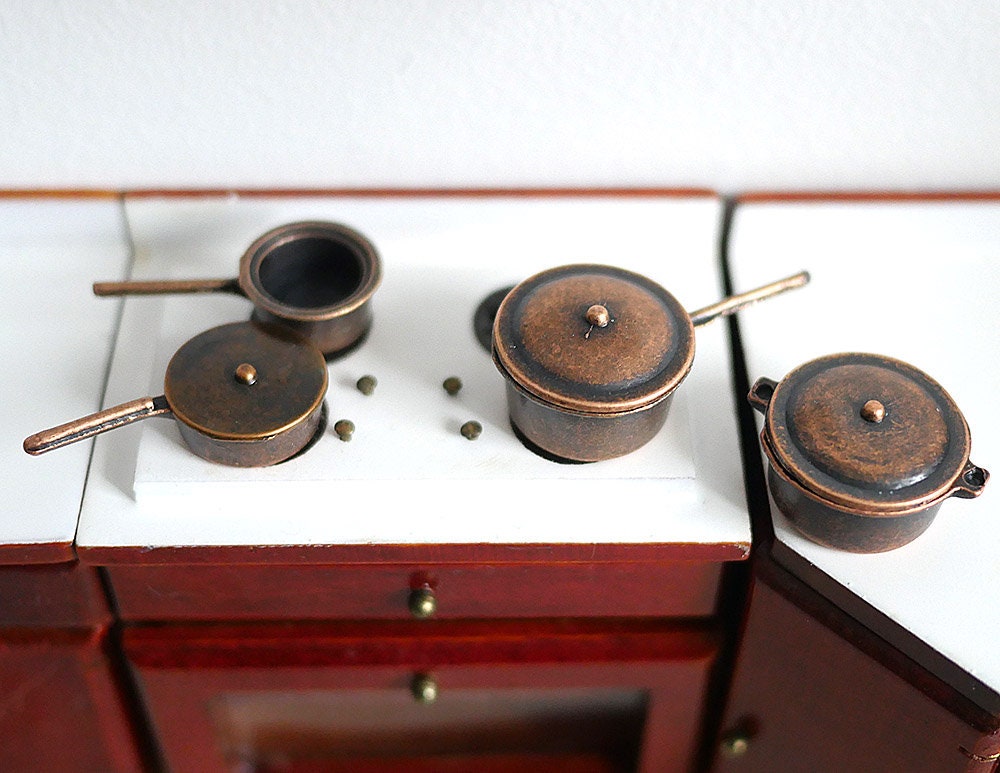 1:12 scale miniature bronze metal cooking pots with lids and handles, set of 4, shown on a white stove top