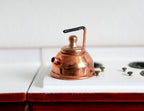 1:12 scale miniature metal kettle in copper with black handle and spout, shown on a white stove top
