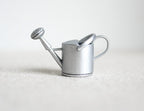 1:12 scale miniature metal watering can in silver with long spout and rose head, shown on a white surface