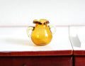 1:12 scale miniature glass jug in amber brown with two handles and ruffled rim, shown on a white counter