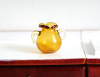 1:12 scale miniature glass jug in amber brown with two handles and ruffled rim, shown on a white counter