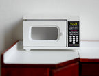 1:12 scale miniature white microwave oven with black window door and keypad, shown on a kitchen counter
