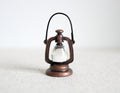 1:12 scale miniature copper metal hurricane oil lantern with wire handle and clear globe, on a white surface