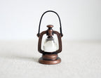 1:12 scale miniature copper metal hurricane oil lantern with wire handle and clear globe, on a white surface