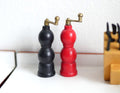 1:12 scale miniature wood salt and pepper mills in black and red with gold crank handles, set of 2, on a white counter
