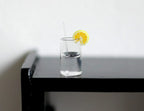 1:12 scale miniature glass of lemon water with ice, clear with a lemon slice and straw, shown on a black table