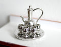 1:12 scale miniature holloware tea set in silver, set of 6 with tall teapot, 4 glasses and round tray, on a white counter
