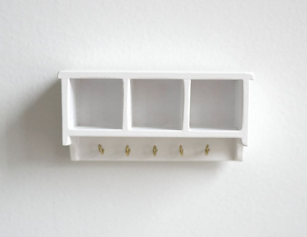 1:12 scale miniature wood wall shelf in white with 3 cubbies and a row of hooks, shown mounted on a white wall