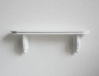 1:12 scale miniature white wood wall shelf with two scroll brackets, shown mounted on a plain white wall