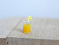 1:12 scale miniature glass of orange juice with lemon slice and straw, shown on a rustic wood table