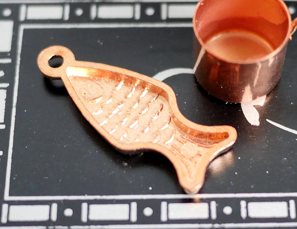 1:12 scale miniature copper metal fish shaped baking mold with hanging loop, shown on a black stove top beside a copper pot