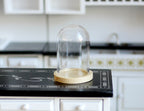 1:12 scale miniature glass dome on round wood base, clear display cloche shown on a black kitchen counter