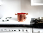 1:12 scale miniature copper plated cooking pot with two side handles and red interior, shown on a white kitchen stove