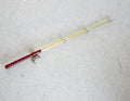 1:12 scale miniature metal fishing rod with reel, red handle and gold rod, shown lying on a white fabric surface