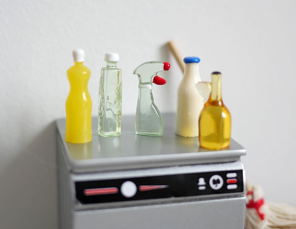 1:12 scale miniature cleaning bottles, set of 5, yellow, clear and cream bottles including a spray bottle, on a washer