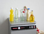 1:12 scale miniature cleaning bottles, set of 5, yellow, clear and cream bottles including a spray bottle, on a washer