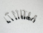 1:12 scale miniature hand tools in black and silver, set of 8, hammer, saw, pliers and wrenches laid out in a row