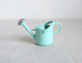 1:12 scale miniature mint green metal watering can with spray nozzle and handle, shown on a linen surface