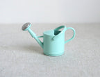 1:12 scale miniature mint green metal watering can with spray nozzle and handle, shown on a linen surface