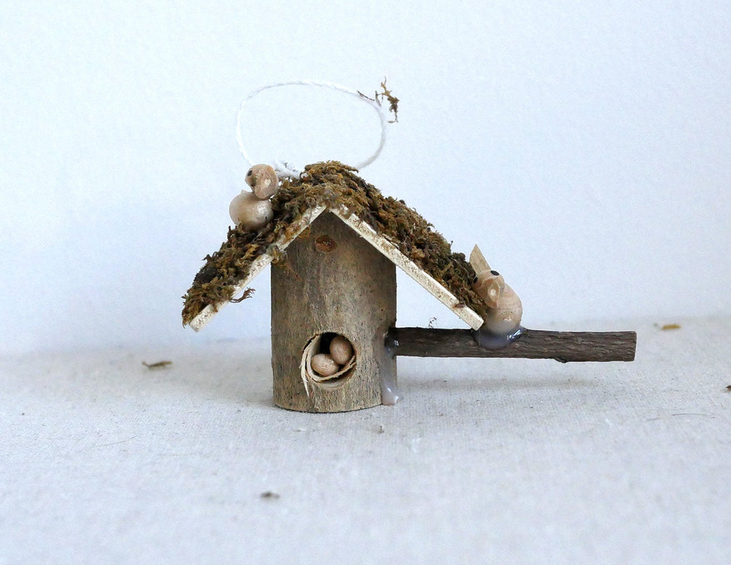 1:12 scale miniature log cabin birdhouse with bark roof and twig perch, shown on a white surface