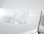 1:12 scale miniature clear tumbler glasses with faceted base, set of 2, one upright and one on its side on a counter