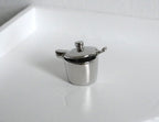 1:12 scale miniature metal sugar bowl with lid and spoon in polished silver, set of 2, shown on a white counter
