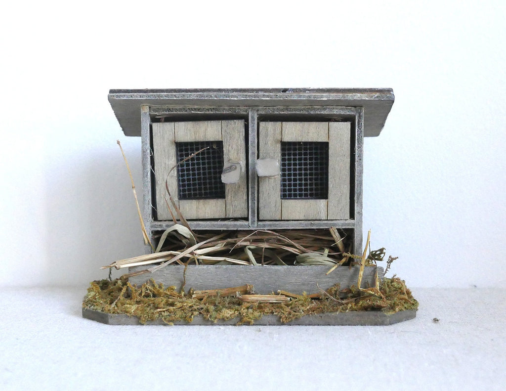 1:12 scale miniature wood chicken coop on straw base in weathered gray with 2 wire mesh doors, on a white background