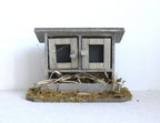1:12 scale miniature wood chicken coop on straw base in weathered gray with 2 wire mesh doors, on a white background