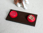 1:12 scale miniature red pet food and water bowls with tray, kibble in one bowl on a dark brown mat, shown by a toy dog