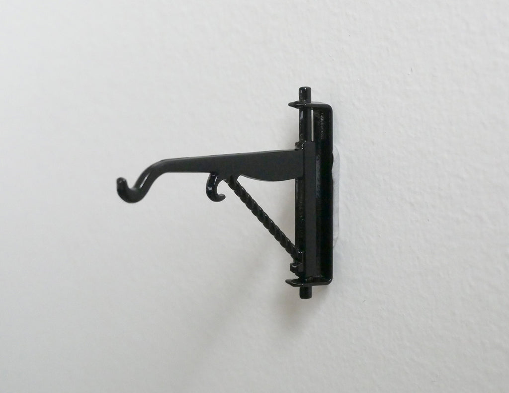 1:12 scale miniature metal hanging wall bracket with hook in black, scroll arm design, shown mounted on a white wall