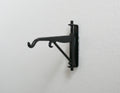 1:12 scale miniature metal hanging wall bracket with hook in black, scroll arm design, shown mounted on a white wall