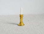 1:12 scale miniature metal candle holder in gold with a white taper candle, shown on a light fabric surface