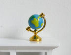 1:12 scale miniature world globe in blue and green on gold metal stand with round base, on a white table